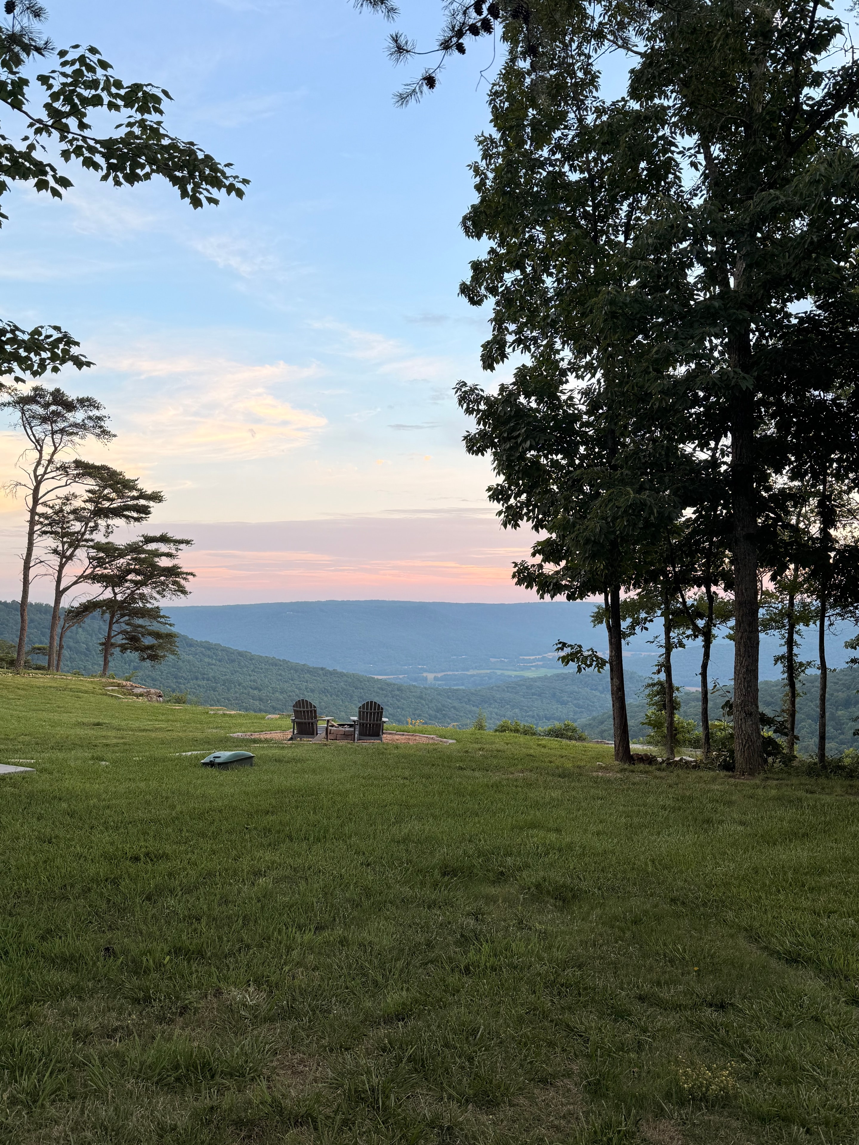 Adirondack chairs overlooking a lake at sunset with pine trees